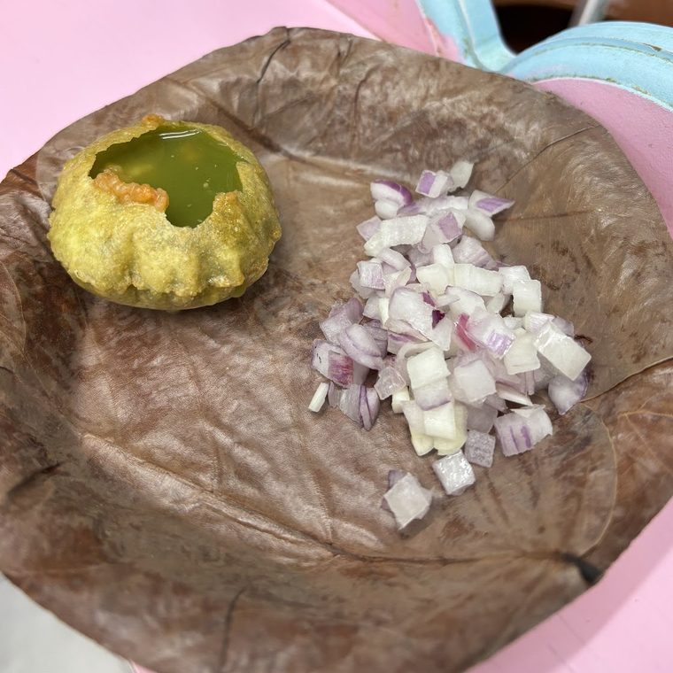 A pani puri filled with green pani, served on a leaf plate with chopped onion